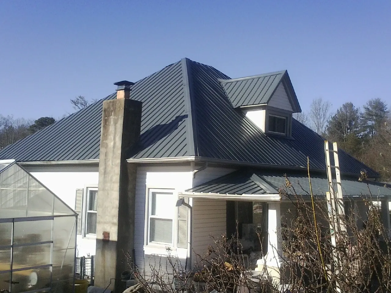 Dark blue standing seam metal roof on a white farmhouse with dormer — Slate & Tile Roof Repair by Roofing Brothers in Indian Hills