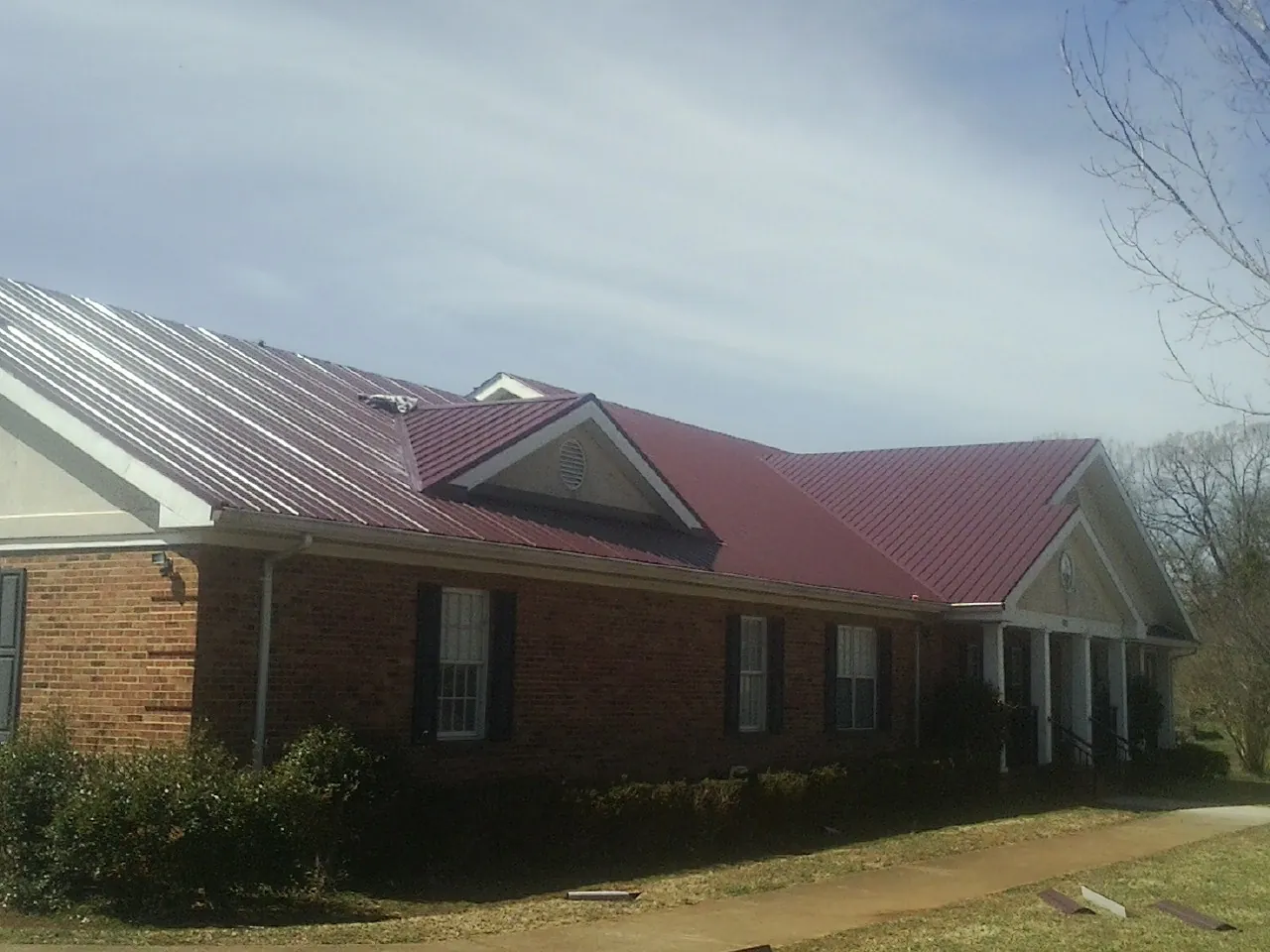 Red metal roof with gabled entries on a long brick building, from a Hail Damage Roof Repair job in Indian Hills