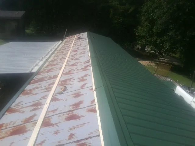 Old rusted panels beside newly installed green metal roofing — Wind Damage Roof Repair by Roofing Brothers in Indian Hills