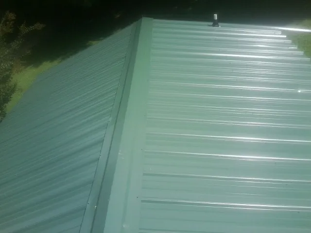 New green metal panels meeting at the ridge of a roof — Flat Roof Repair work by our crew in Indian Hills