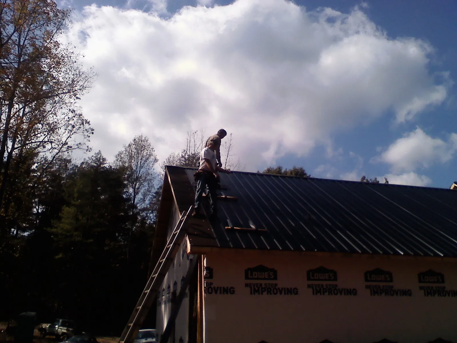 Roofer fastening dark metal panels high against a cloudy sky, from a Roof Inspection job in Indian Hills