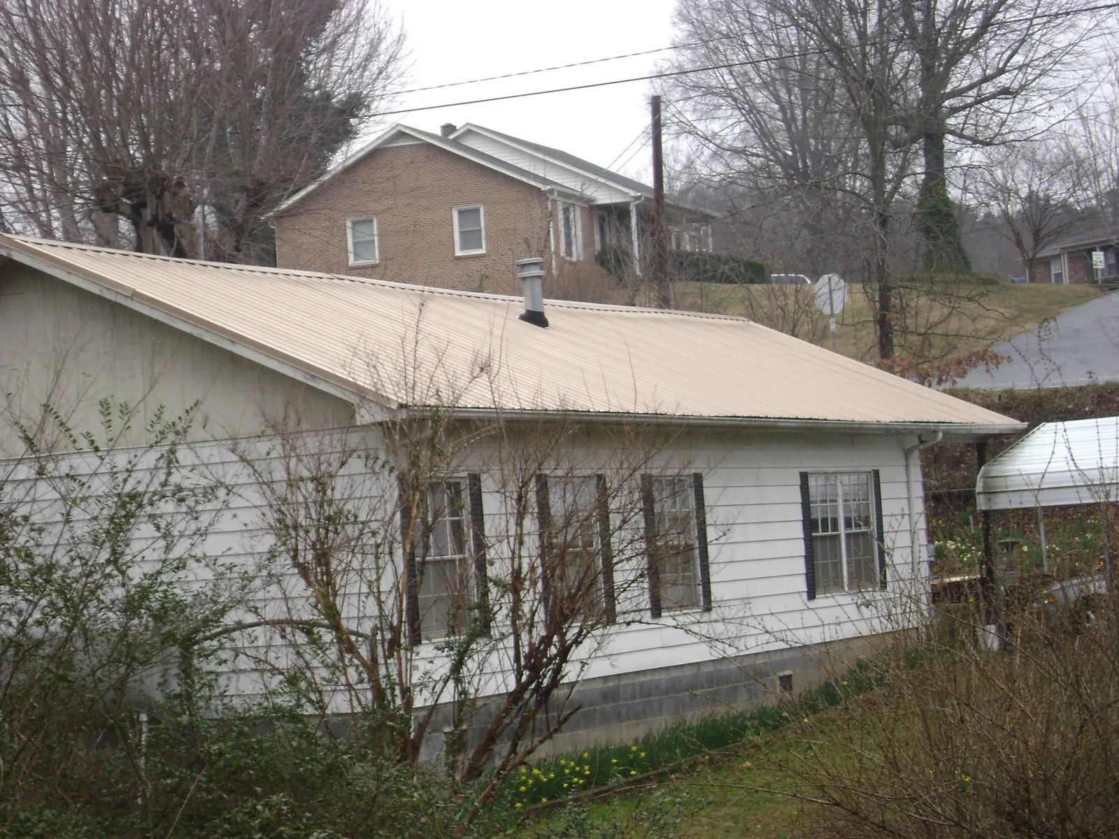 Tan metal roof on a white sided house set into a hillside — Commercial Roofing by Roofing Brothers in Indian Hills