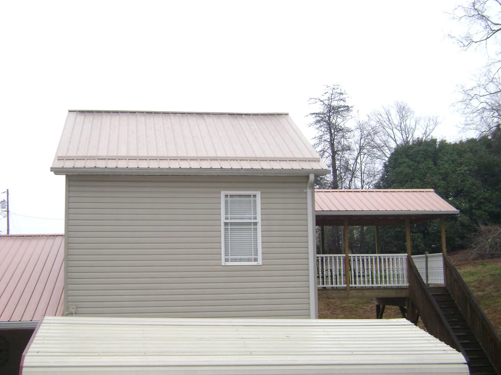 Tan metal roofs on a two story addition and attached porch, from a Roof Replacement job in Indian Hills